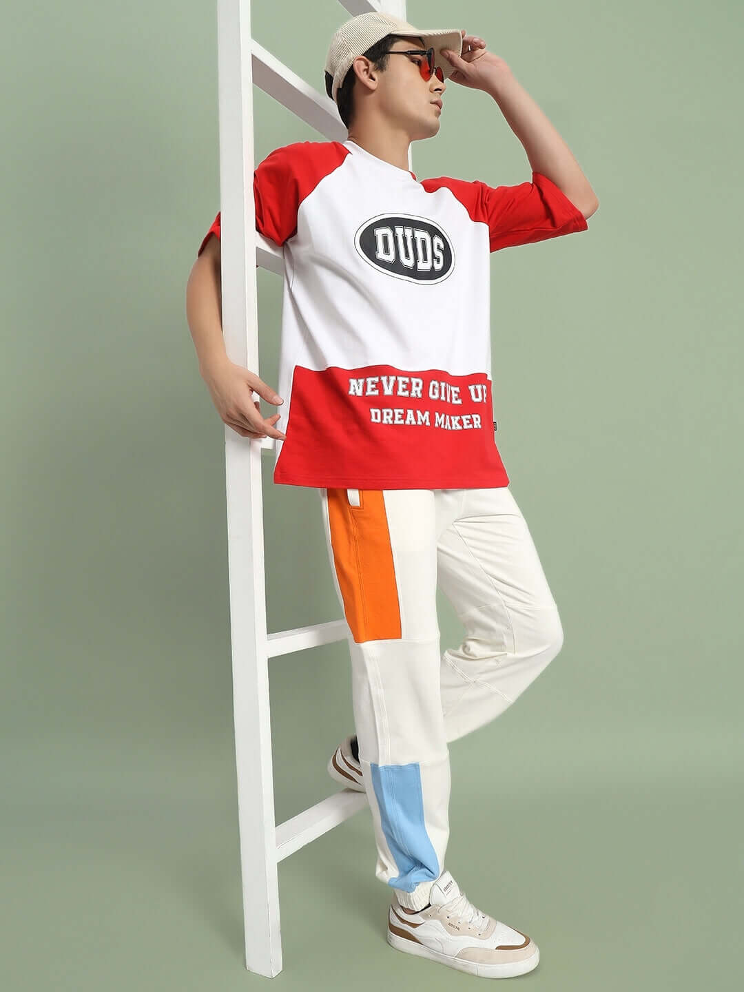 Model wearing DUDS Parker Side Contrast Joggers in off-white with colorful panels, styled with a red and white shirt and casual sneakers.