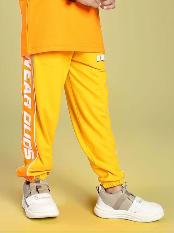 Child wearing PEPPY JOGGER FOR BOYS AND GIRLS ORANGE with white sneakers on a yellow background.