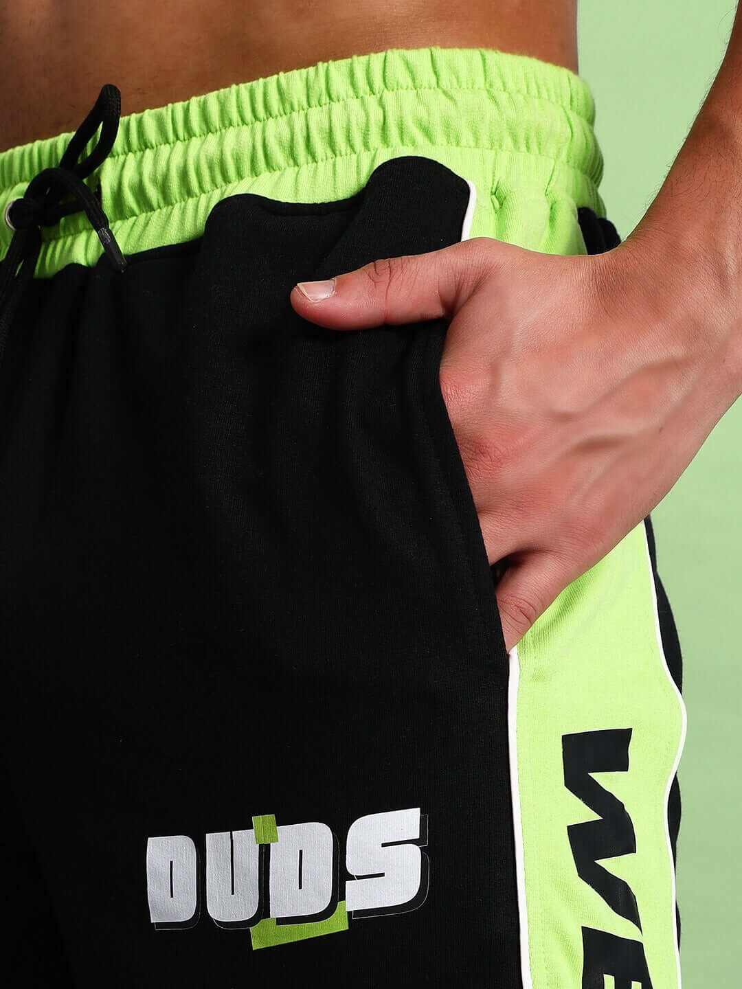 Close-up of black and neon green PEPPY joggers with DUDS logo, featuring adjustable waistband and side stripe detail.