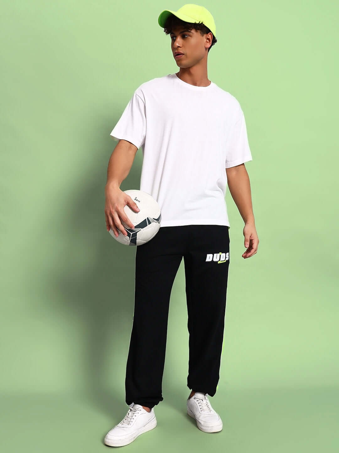 Man wearing PEPPY JOGGERS in Black-Neon Green by DUDS, holding a soccer ball, standing against a green background.