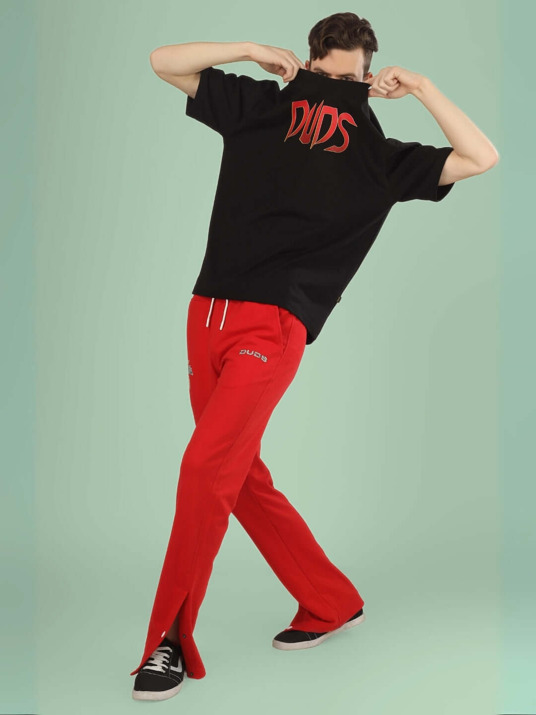 Model wearing red Phoenix digital printed joggers by DUDS, lifting a black shirt to reveal the brand name, stylish and comfortable fit.