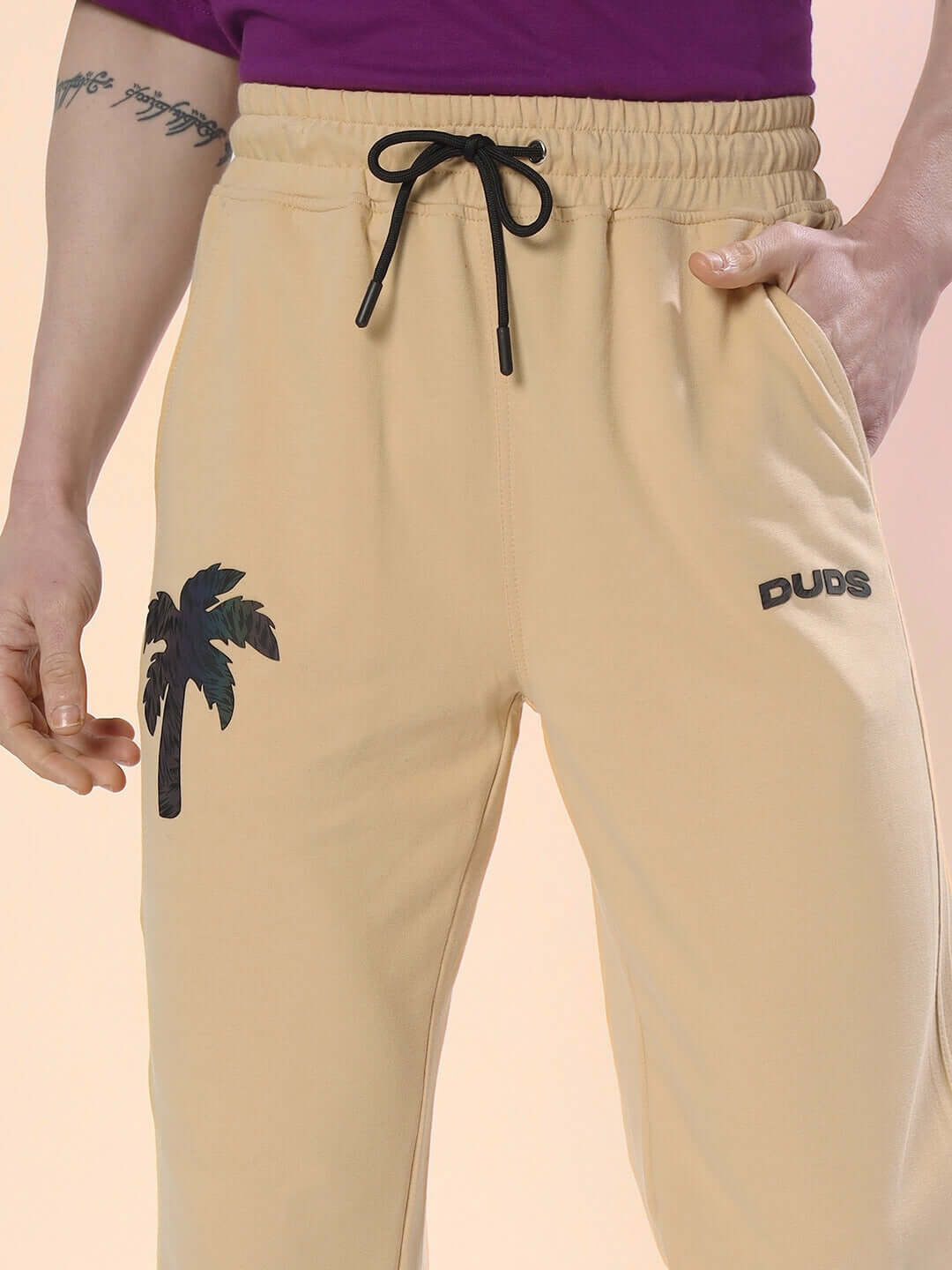 Beige digital printed joggers by DUDS featuring a palm tree design, customizable fit available, model wearing purple top.