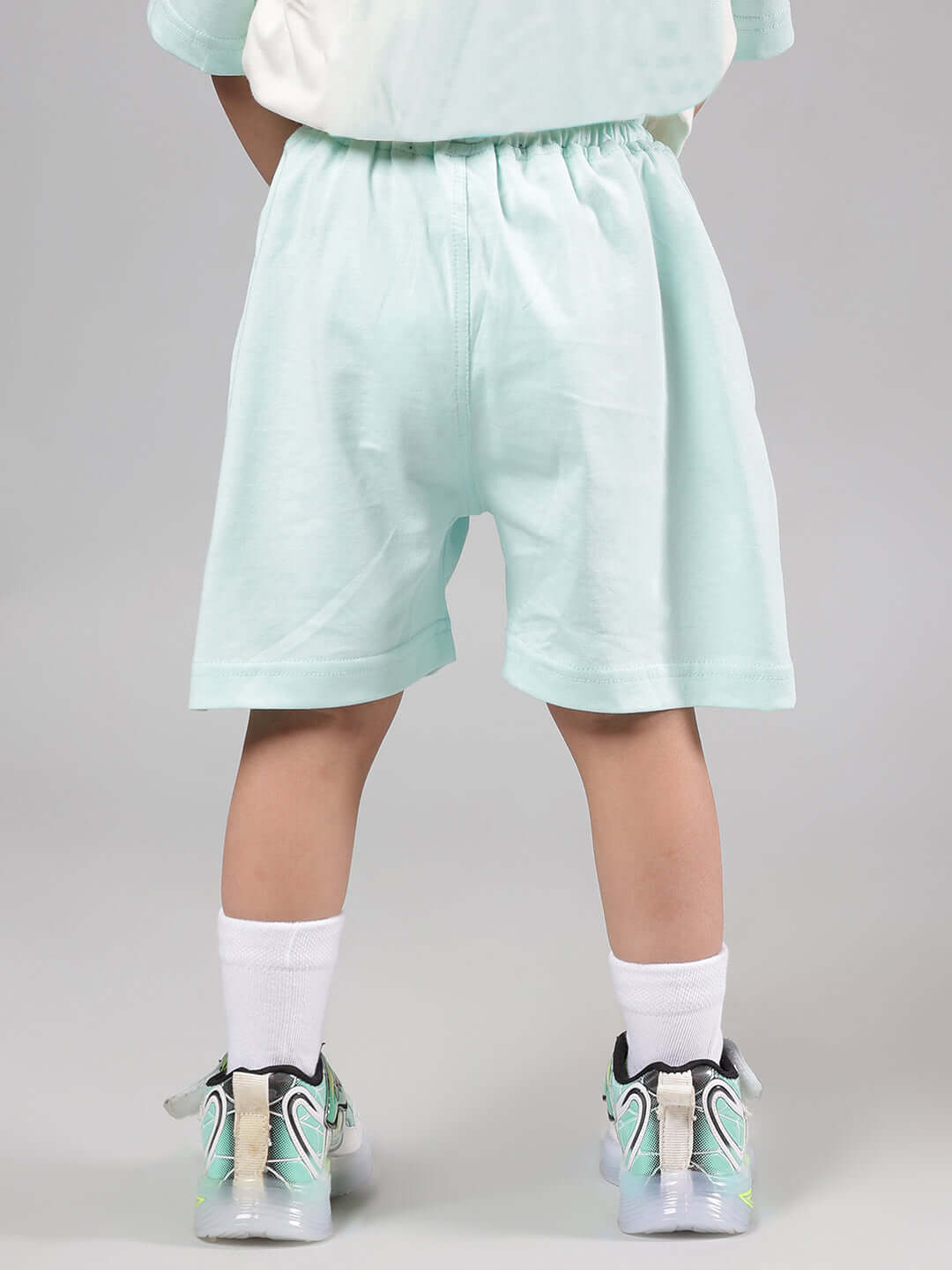 Child wearing Piano Bird Shorts for Boys Girls Sky Blue, showing back view of light blue shorts paired with playful shoes.