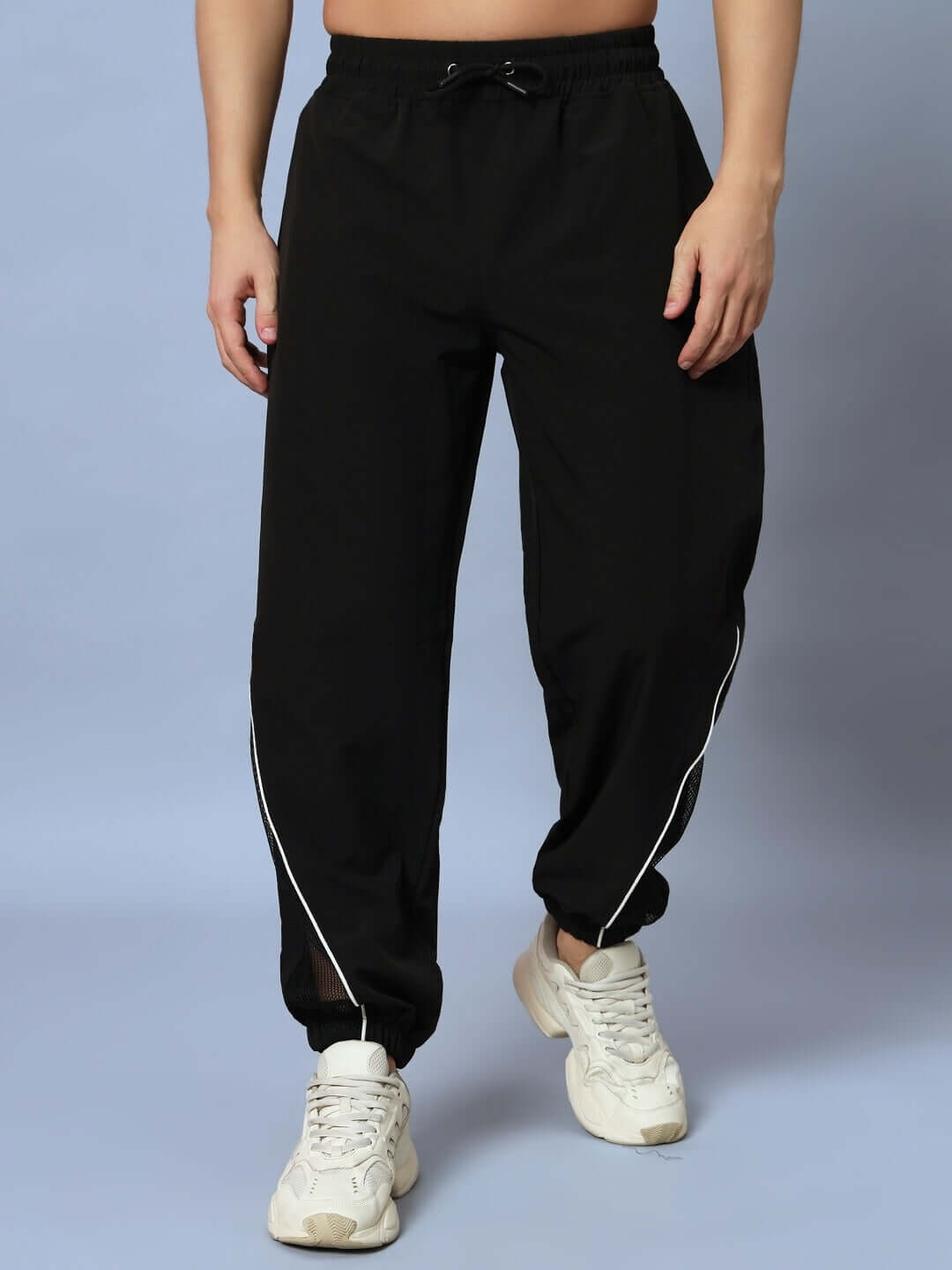 Person wearing black joggers with white sneakers on a neutral background