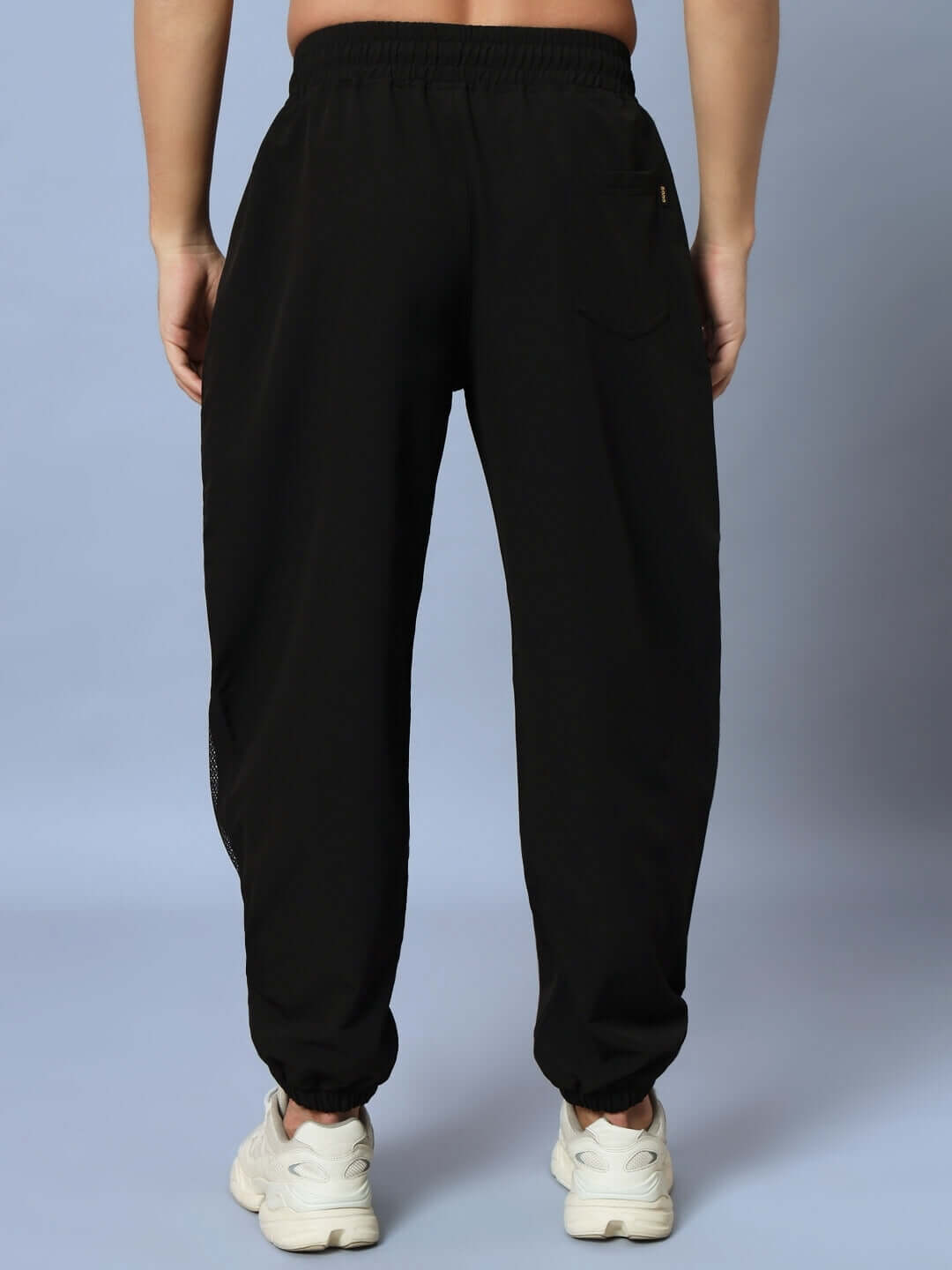Back view of black PLEXUS joggers showcasing relaxed fit, made-to-order by DUDS, paired with white sneakers.
