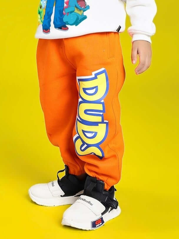 Child wearing POKEMON TOON FLEECE JOGGER FOR BOYS AND GIRLS ORANGE with cartoon design and sneakers on yellow background.