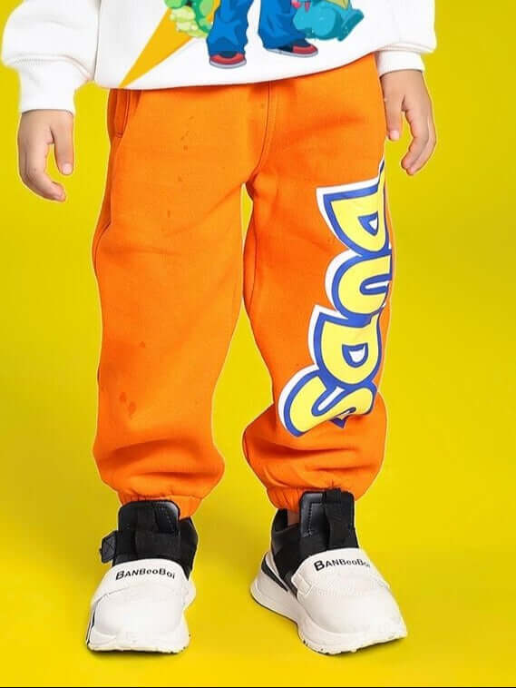 Child wearing POKEMON TOON FLEECE JOGGER FOR BOYS AND GIRLS ORANGE with cartoon design and sneakers on yellow background.