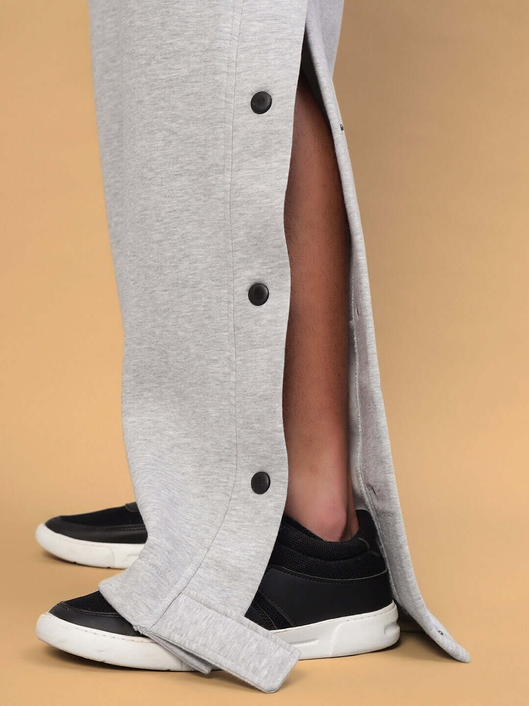 Side view of grey Polar Cotton Fleece Jogger showcasing button details, worn with black sneakers on a beige background.