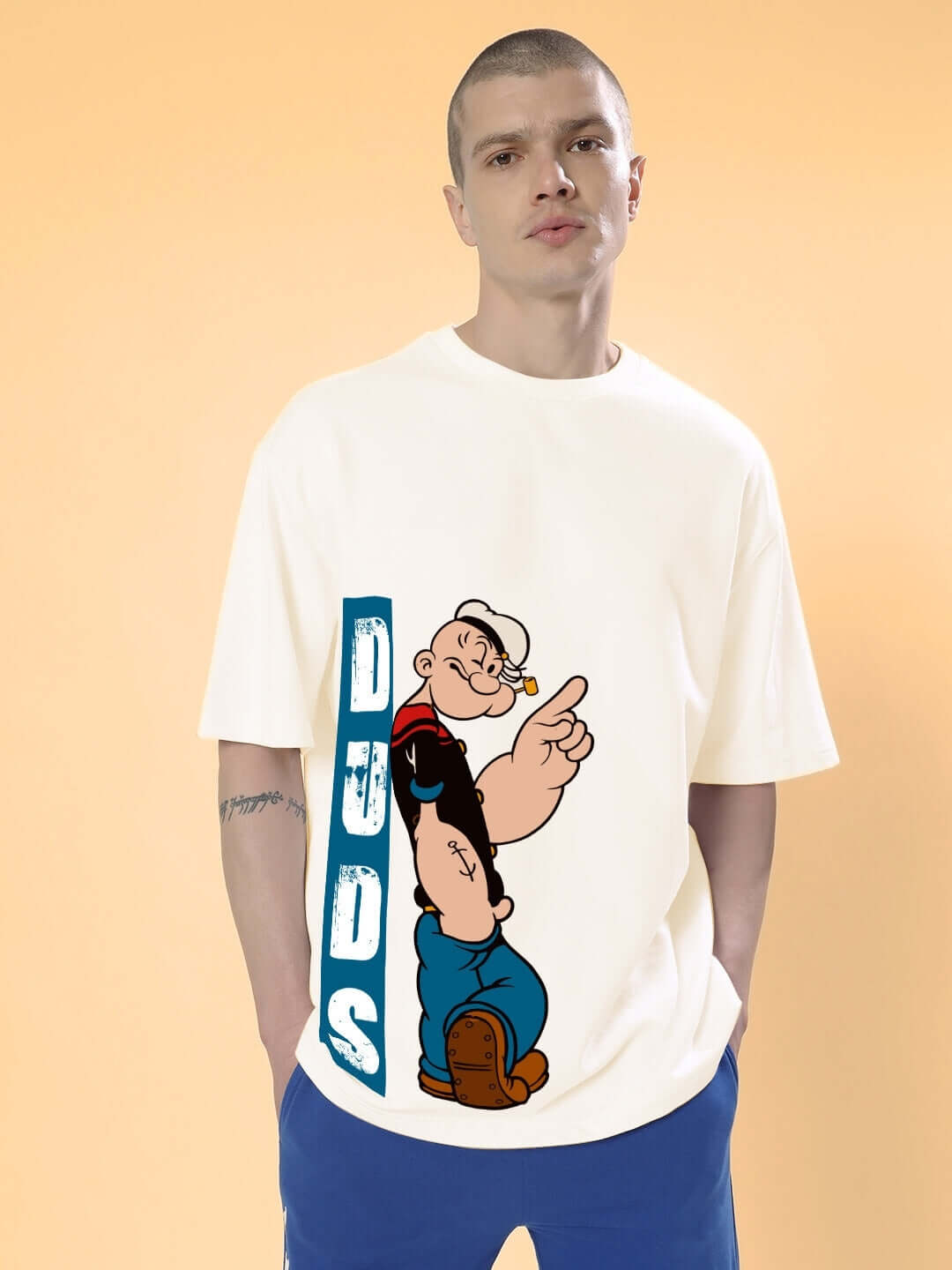 Man wearing a cream oversized t-shirt featuring a Popeye graphic from DUDS, highlighting customization options.