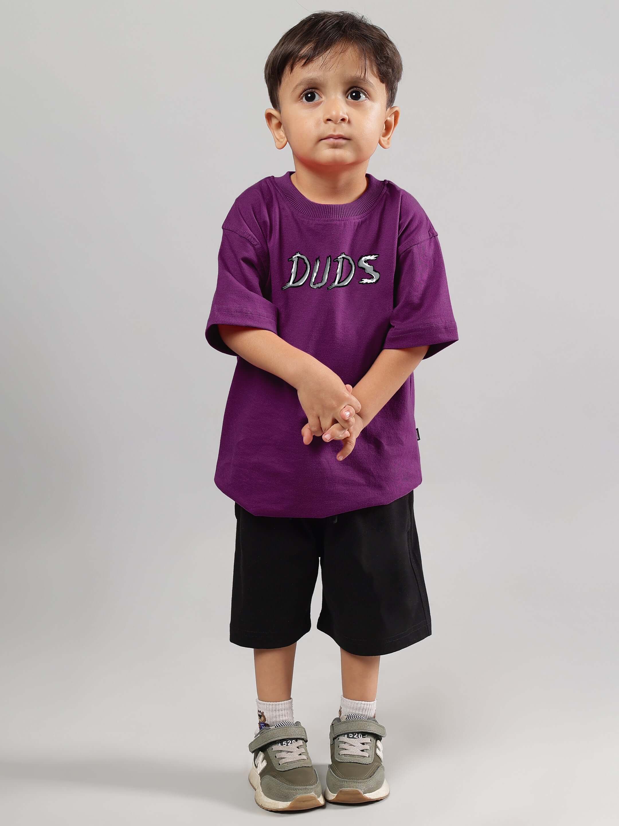 Child wearing a purple DUDS positive rabbit t-shirt for boys and girls, styled with black shorts and sneakers.