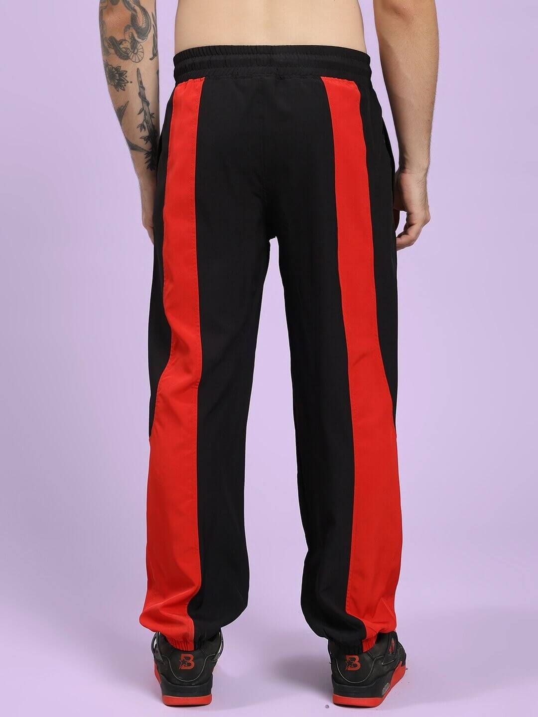 POWER BLOCK RELAXED FIT JOGGER BLACK RED Black track pants with red stripes worn by a person on a light purple background