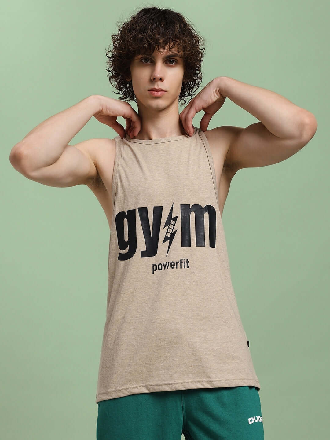 Man wearing a beige Powerfit fitness gym t-shirt with bold 'gym' logo, posing confidently against a green background.