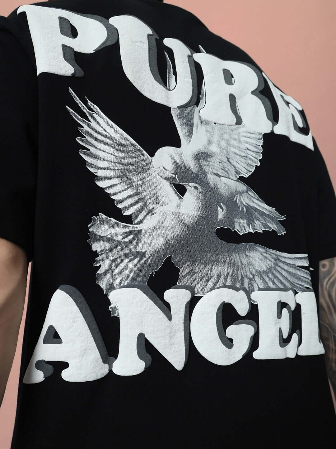 Black oversized t-shirt with 'PURE ANGEL' text and dove print, made from premium cotton, designed by Color By Colours, photo background pink.