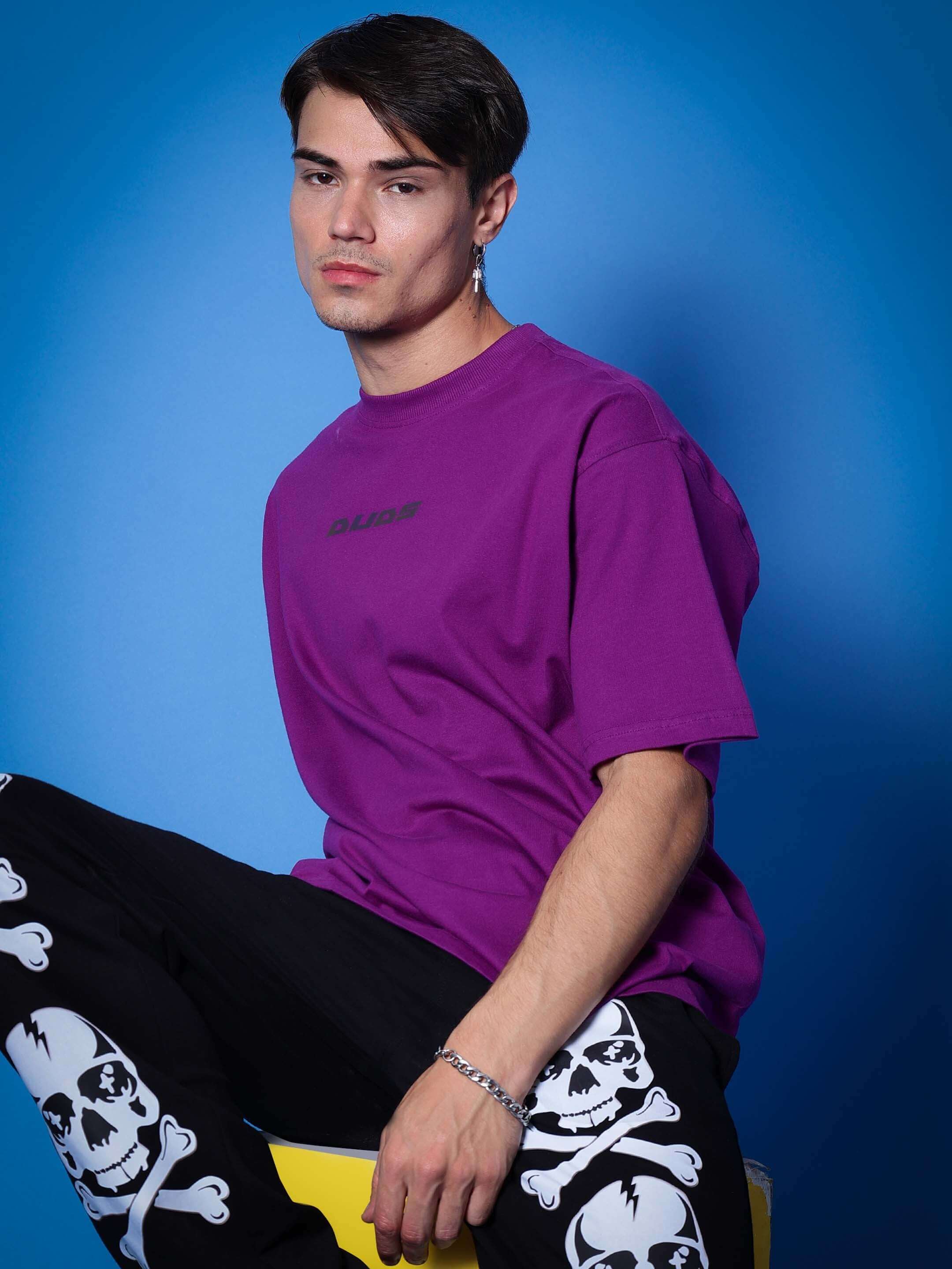 Model wearing DUDS purple t-shirt and black joggers with skull print, posing against a blue backdrop.