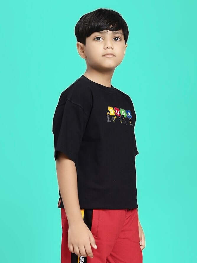 Child wearing PUZZEL T-SHIRT FOR BOYS AND GIRLS BLACK with colorful design, standing against teal background.