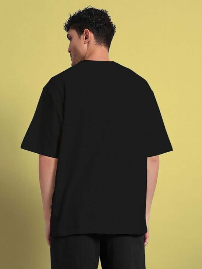 Back view of man wearing QUACK OFF OVERSIZED T-SHIRT BLACK in breathable cotton, showcasing relaxed fit and durable stitching.
