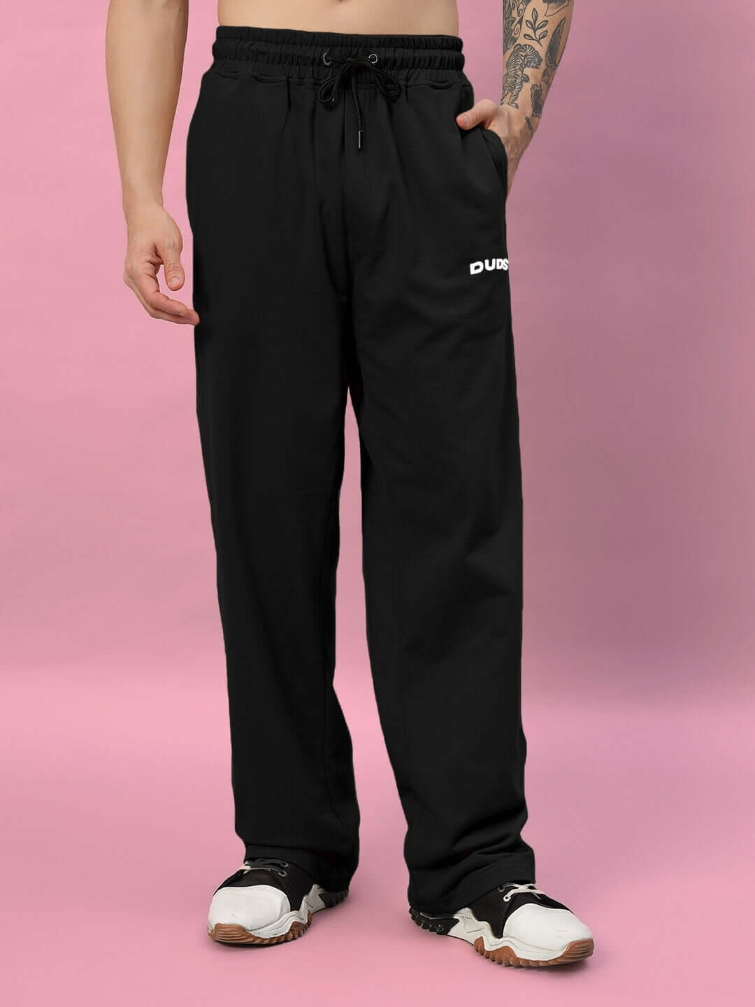Black relaxed-fit joggers by DUDS, featuring a comfortable drawstring waist, tailored fit, and a sleek design on a pink background.