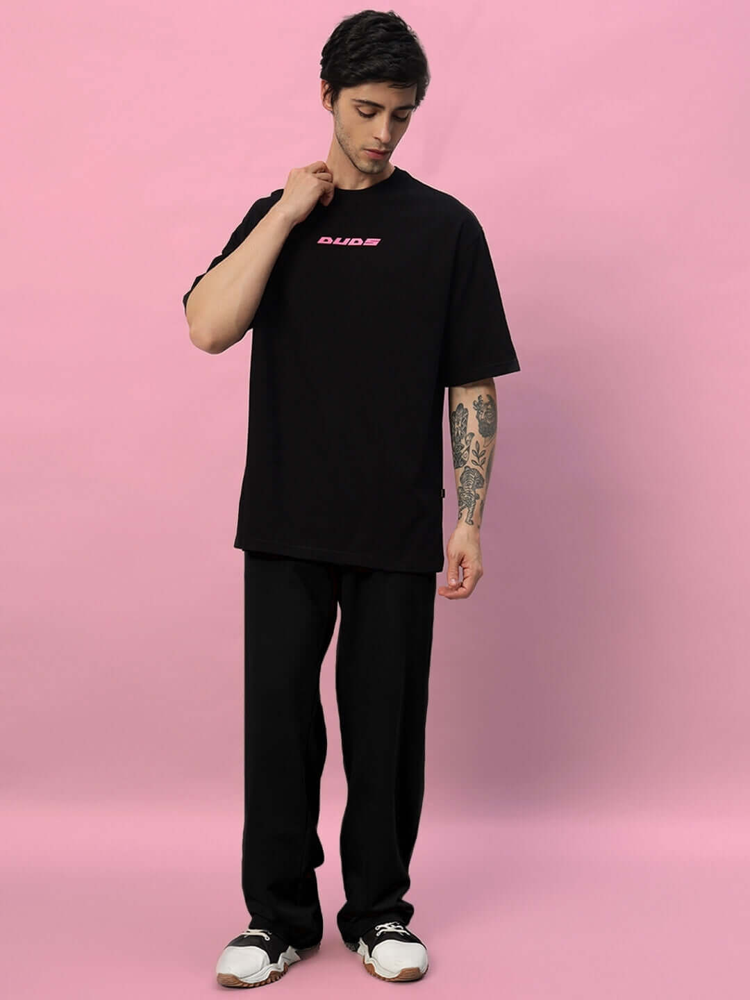 Person wearing Quantum Relaxed-Fit Joggers in black on a pink background, showcasing casual and comfortable fashion by DUDS.