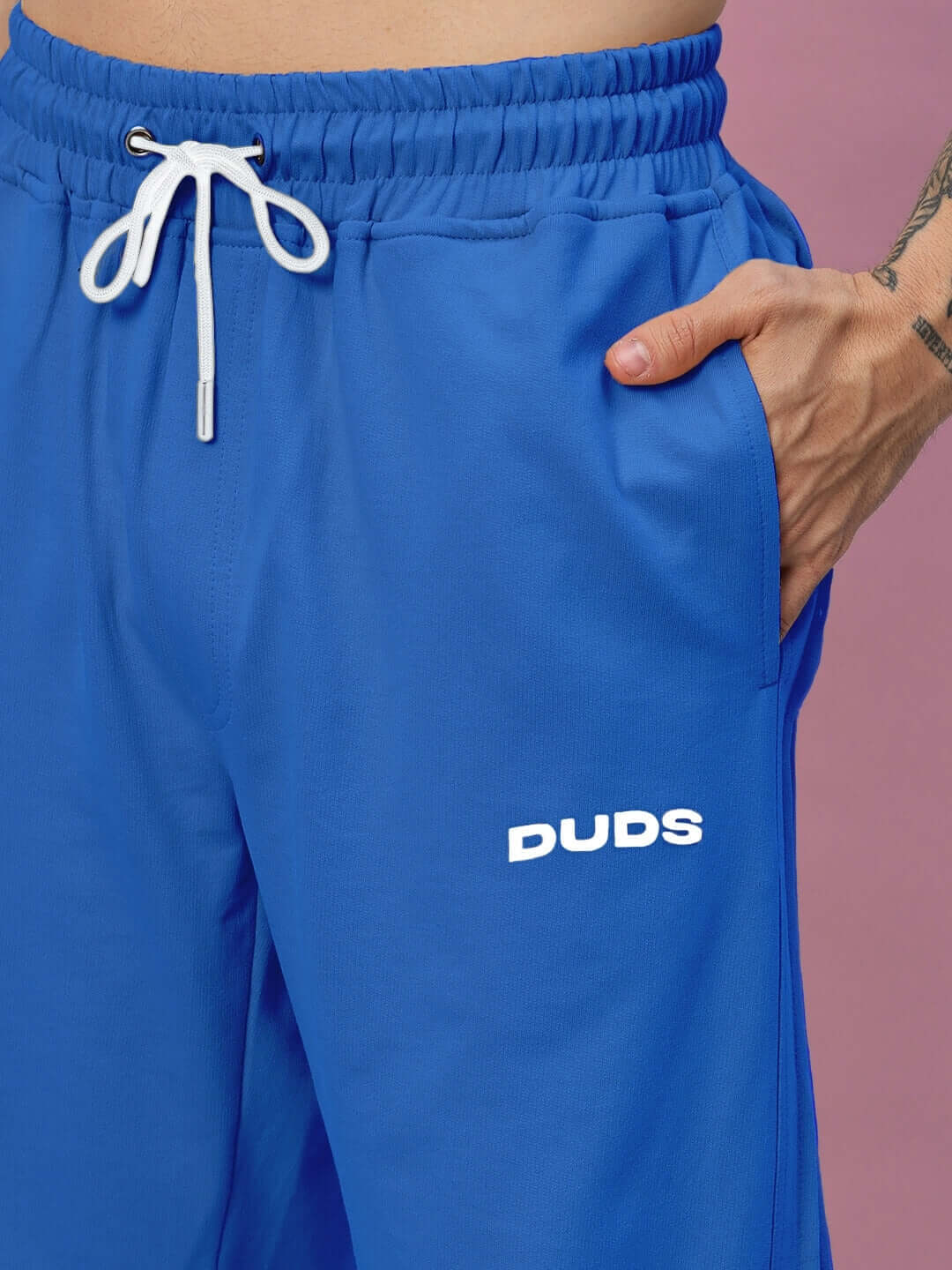 Blue Quantum Relaxed-Fit Joggers by DUDS with drawstring waist, shown close-up on a model against a purple background.