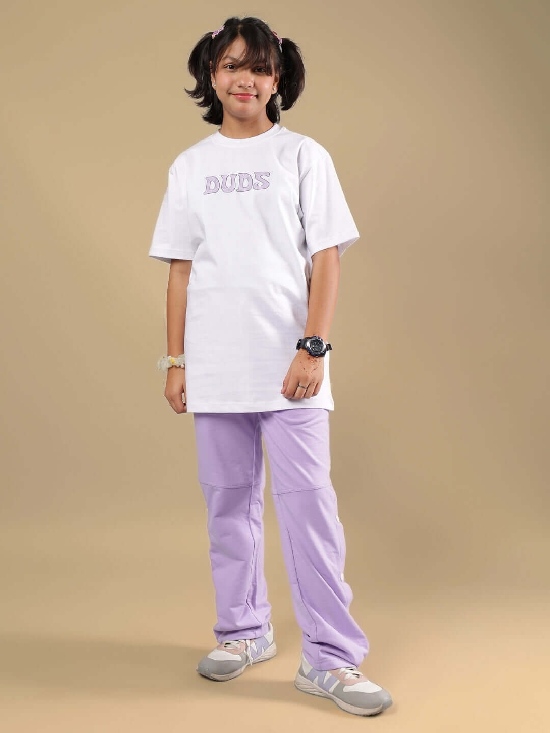 Child wearing RACER JOGGER FOR BOYS & GIRLS LAVENDER with white DUDS shirt, standing and smiling against neutral background.
