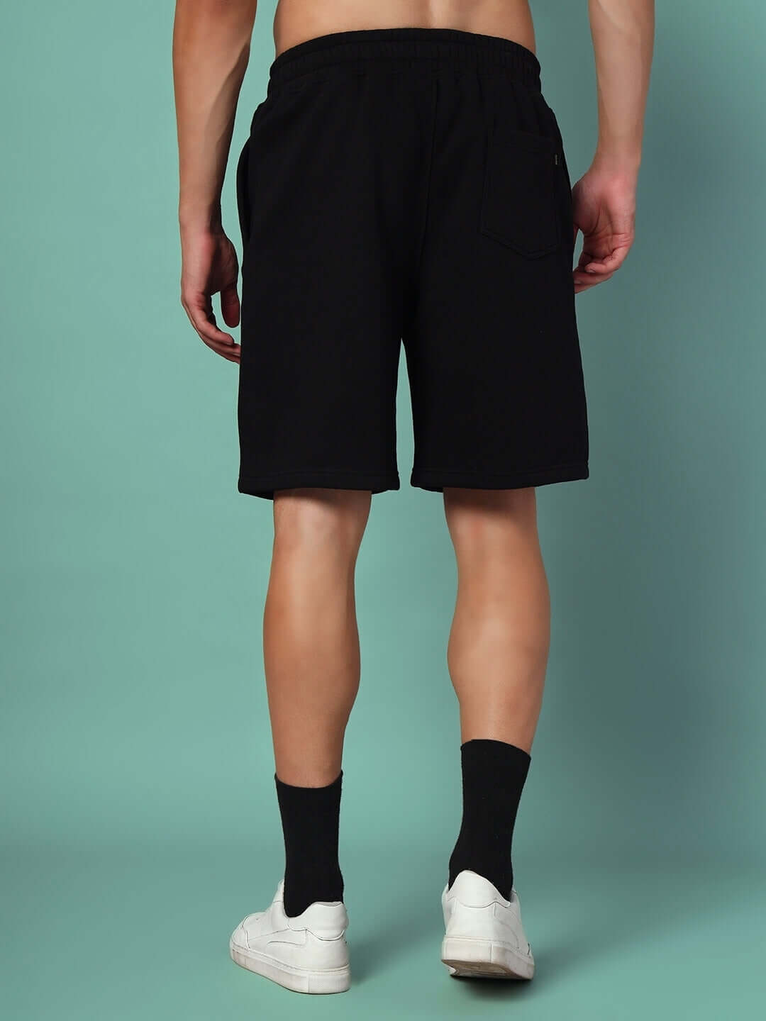 Back view of person wearing black shorts from RACING FOX FLEECE CO-ORD WHITE BLACK with white shoes on teal background.