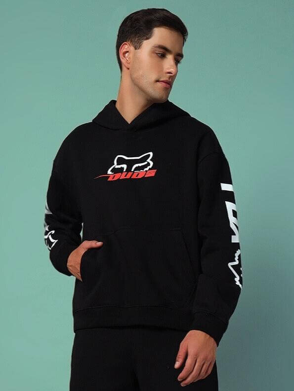 Man wearing Racing Fox Cotton Fleece Hoodie Black, featuring logo design, streetwear style, and roomy hood against a turquoise background.
