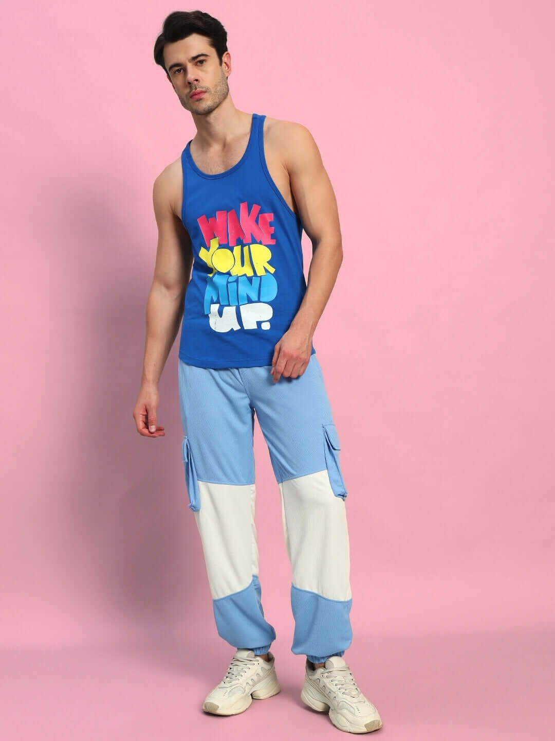Man wearing Radiant Relaxed Fit Joggers, white and sky blue, styled with graphic tank top, on pink background. Made by DUDS.