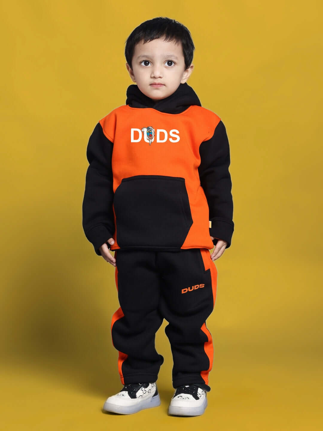 Child wearing RAFIKI CO-ORD FOR BOYS GIRLS BLACK ORANGE with playful design, standing against a yellow background.