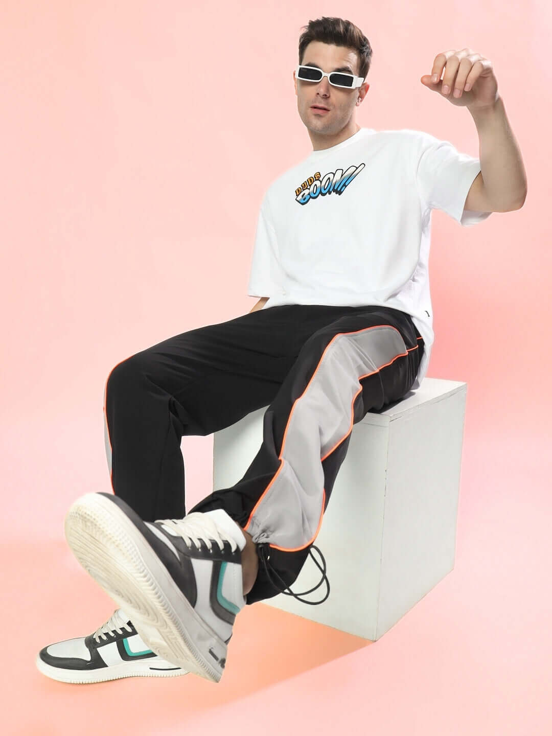 Model wearing RAGE relaxed fit black-grey cargo pants with white sneakers, showcasing street style on a pink background.