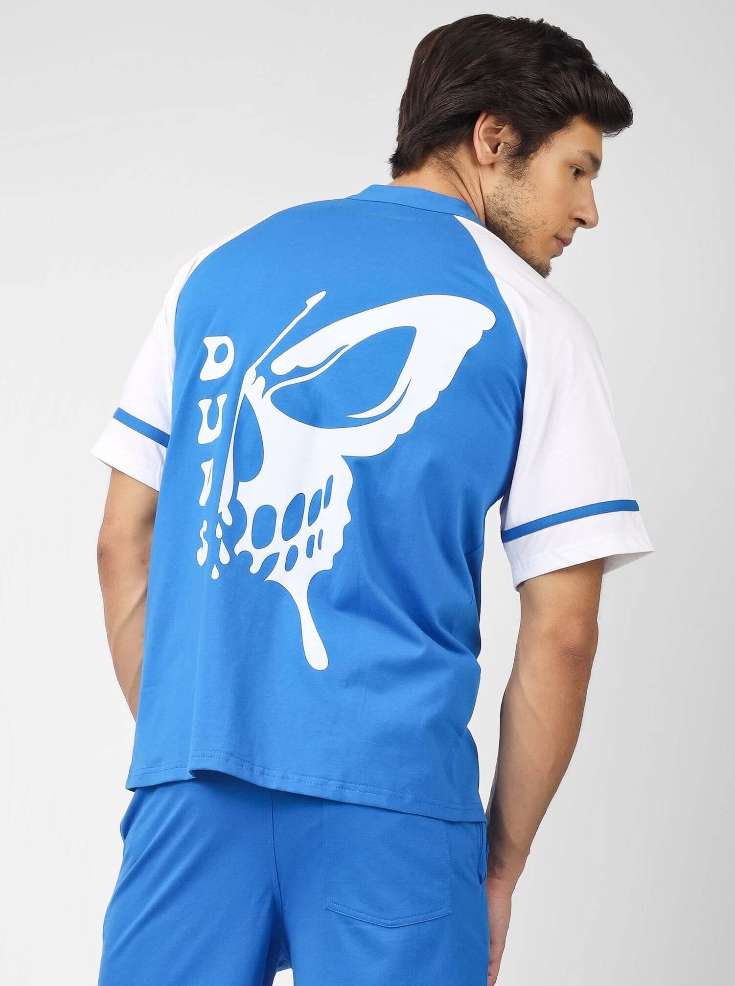 Man wearing RAGLAN OS T-SHIRT WITH SKULL BUTTERFLY PRINT BLUE from back view, featuring large white skull design.