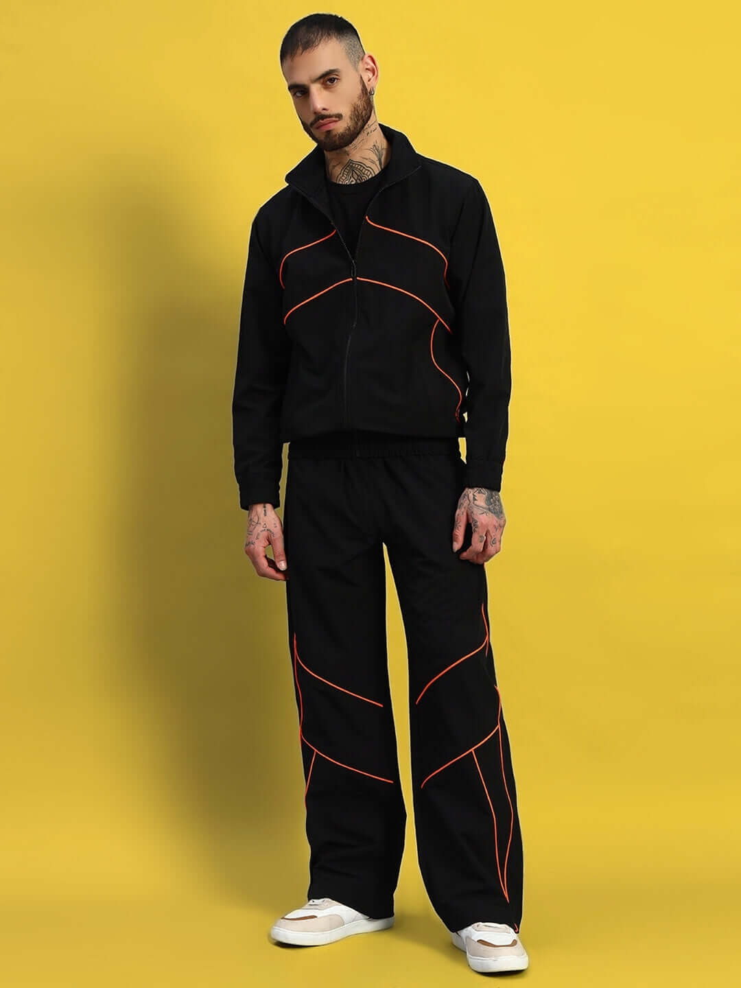 Man wearing a stylish black tracksuit with orange accents, standing against a yellow background.