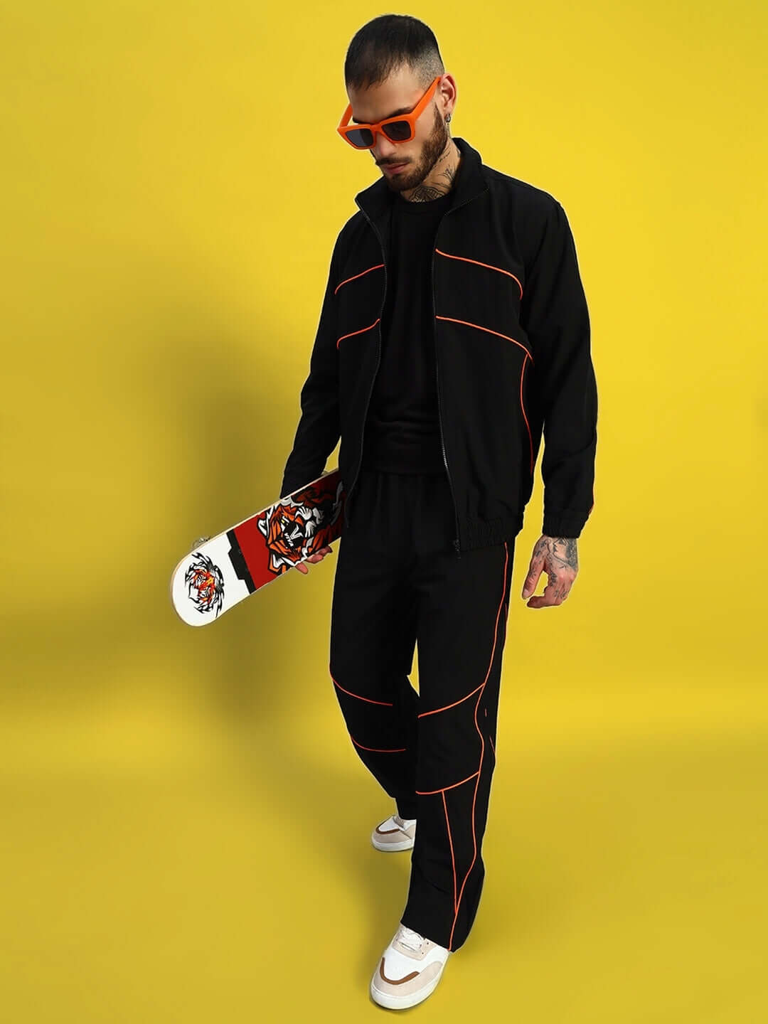 Man wearing black RAIDER RELAXED PANT JOGGER with red trim, holding skateboard against yellow background, sporting sunglasses.