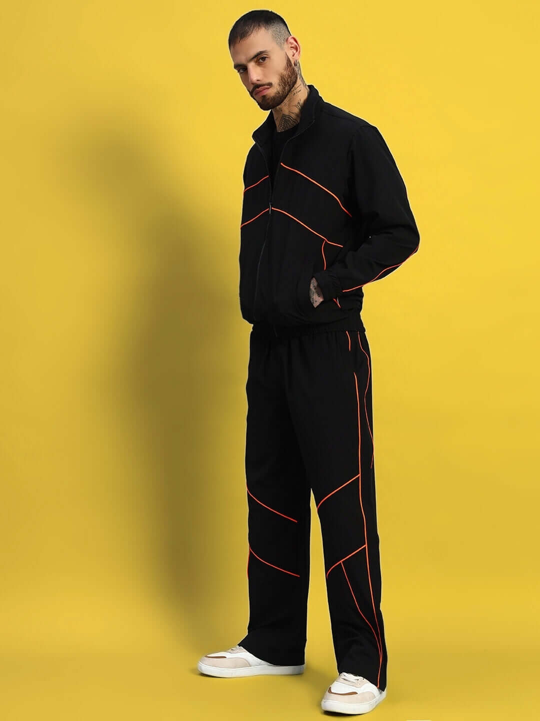 Man wearing Raider Relaxed Pant Jogger in black with orange piping, standing against a yellow background.