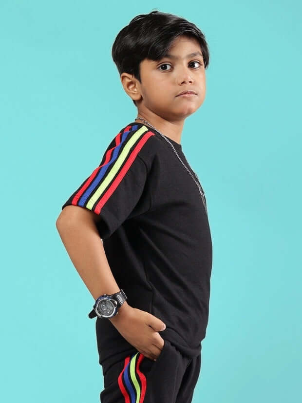 Child wearing RAINBOW OVERSIZED T-SHIRT FOR BOYS & GIRLS BLACK with colorful stripes, standing against a blue background.