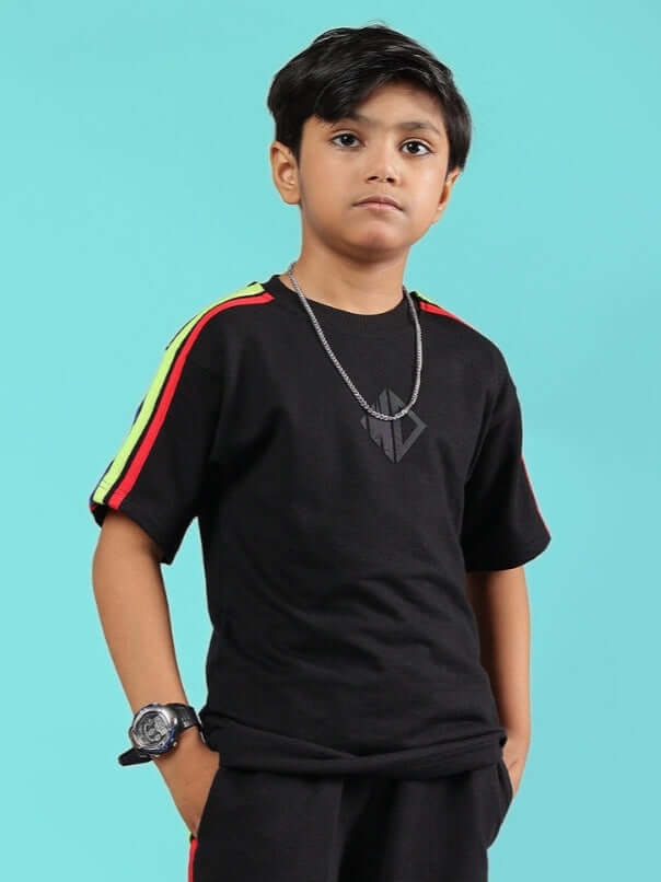Child wearing RAINBOW OVERSIZED T-SHIRT FOR BOYS & GIRLS BLACK with colorful stripes on sleeves against blue background.