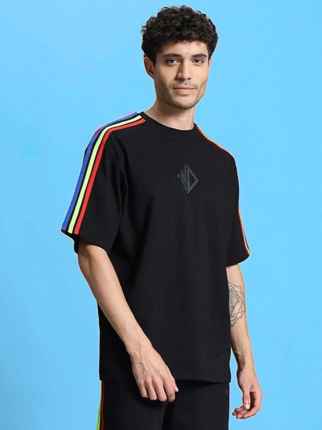 Model wearing RAINBOW OVER-SIZED T-SHIRT BLACK with colorful stripes on black fabric, made from premium heavy gauge cotton blend.