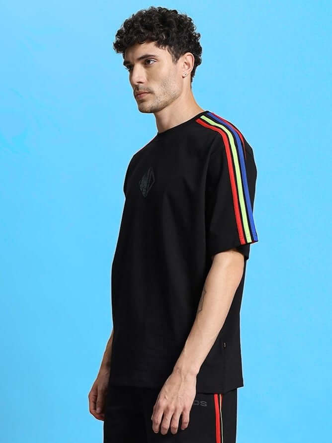 Rugged model wearing RAINBOW OVER-SIZED T-SHIRT BLACK with rainbow shoulder stripes, made of premium cotton blend fabric.