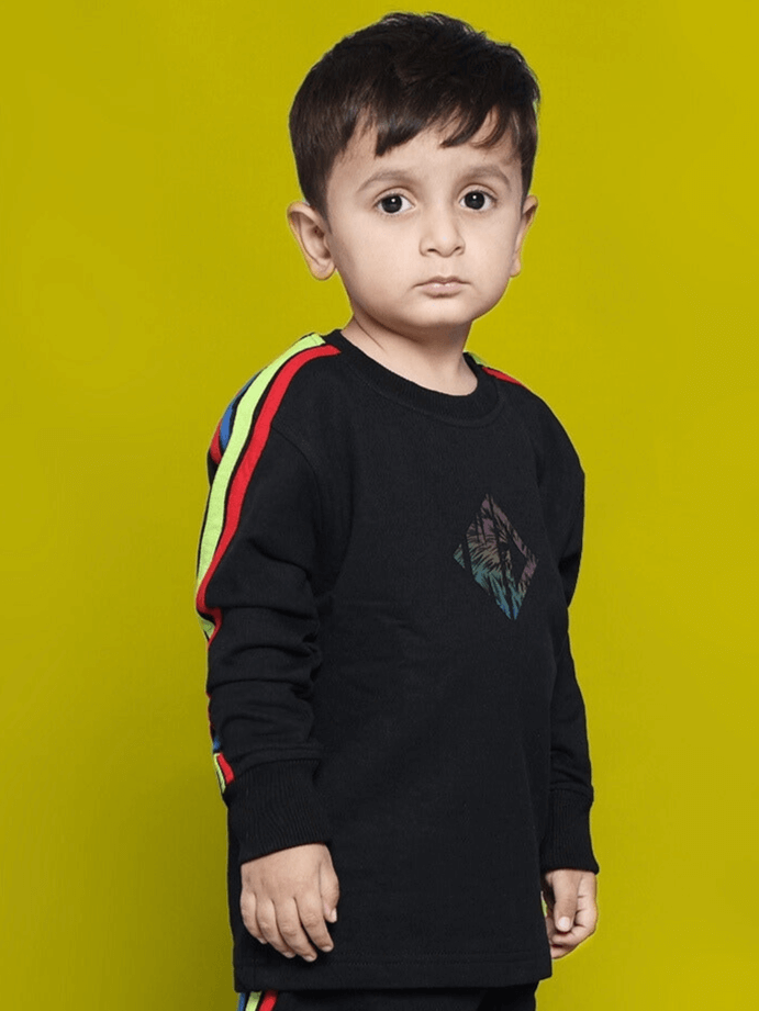 Child wearing RAINBOW OVERSIZED SWEATSHIRT BOYS & GIRLS BLACK with colorful stripes, against a yellow background.