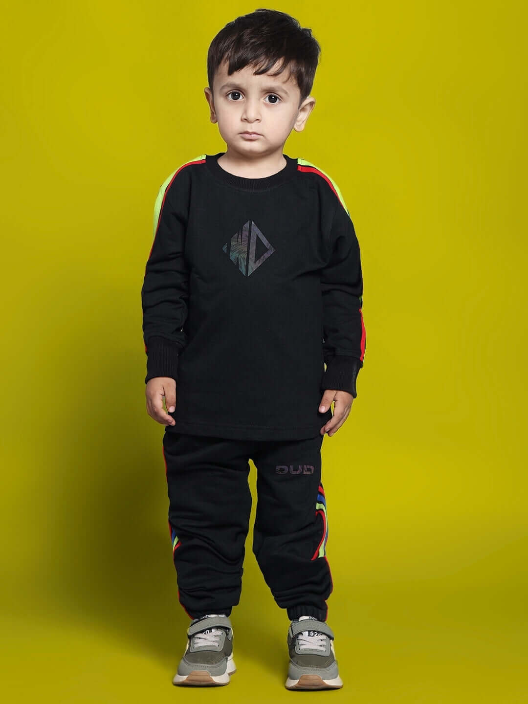 Child wearing black rainbow co-ord set for boys and girls by DUDS, featuring colorful stripes on a bright yellow background.