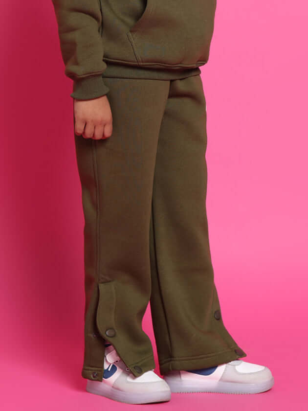 Child wearing olive green rare edition fleece pants with sneakers against a vibrant pink background.