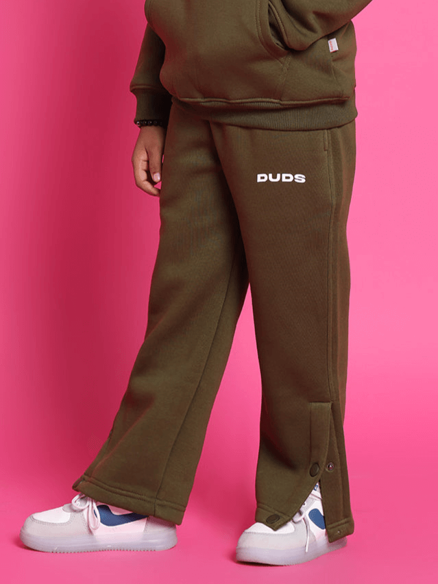 Rare edition fleece pants in olive green for boys and girls, featuring button details, shown against a pink background.
