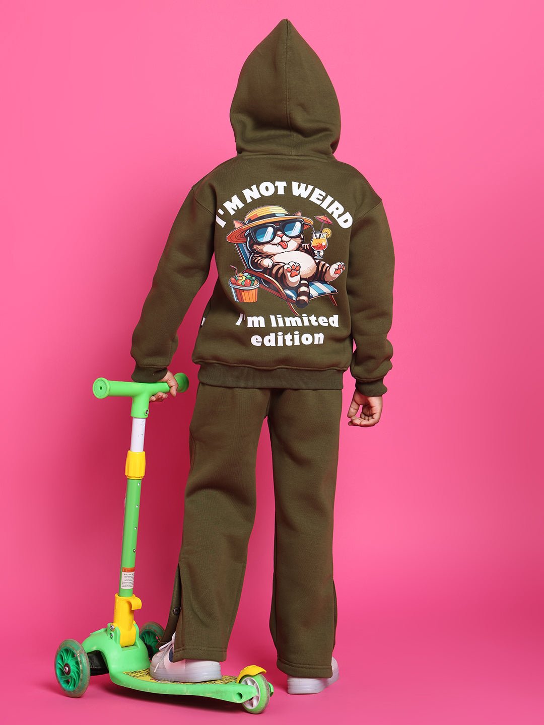 Child wearing RARE EDITION CO-ORD FOR BOYS GIRLS OLIVE GREEN with graphic hoodie, standing by a green scooter on a pink background.
