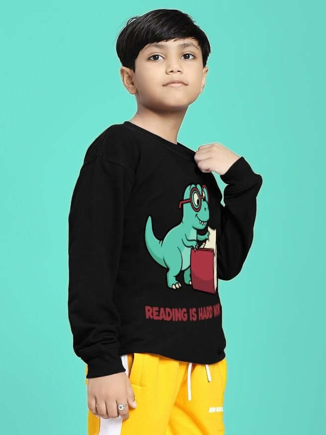 Kid wearing READING HARD PRINTED SWEATSHIRT FOR BOYS GIRLS BLACK with playful graphic, standing in front of a teal background.