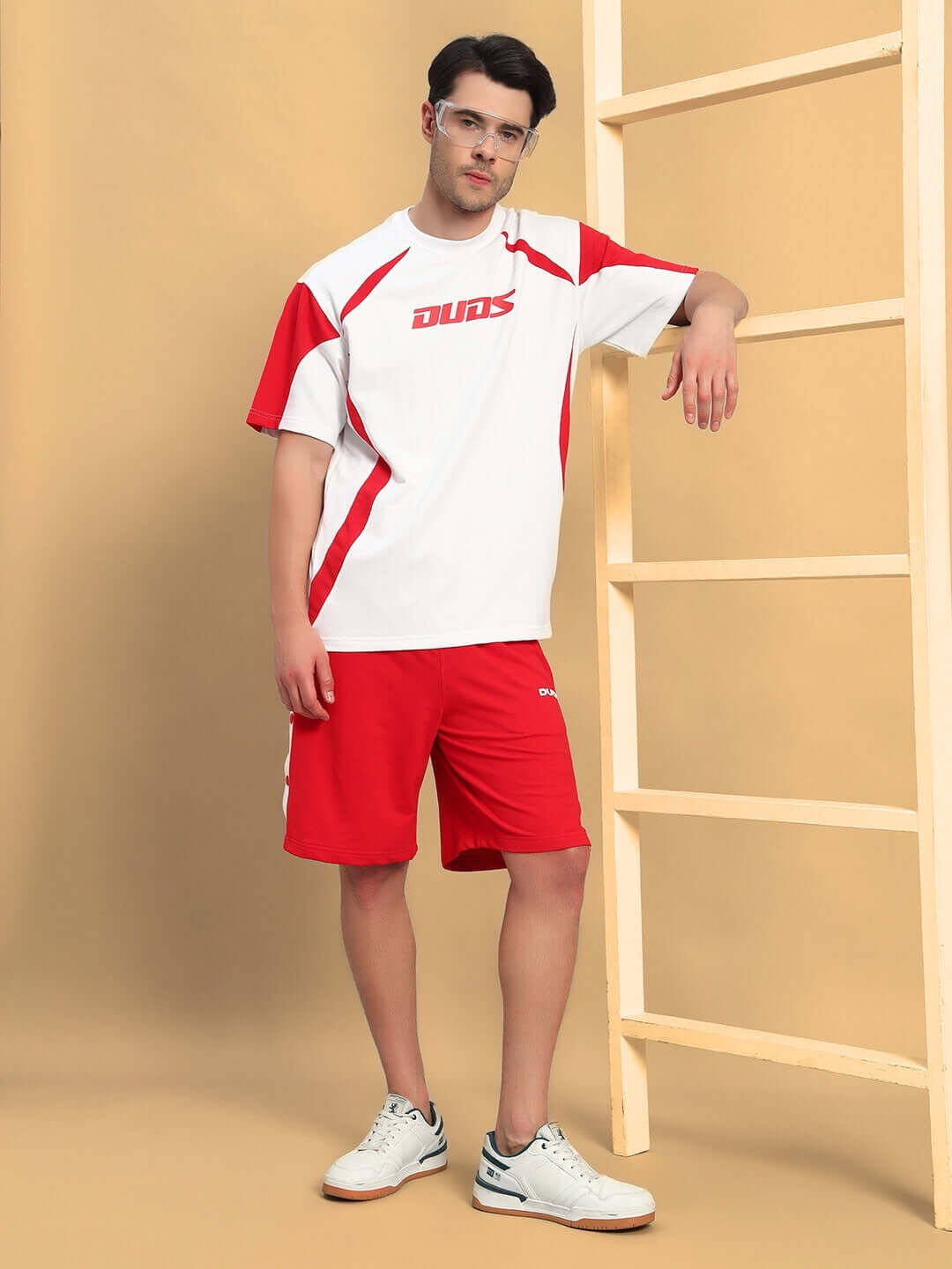 Man wearing EZEL REGULAR FIT COTTON SHORTS RED styled with a matching white and red tee standing by a wooden ladder.