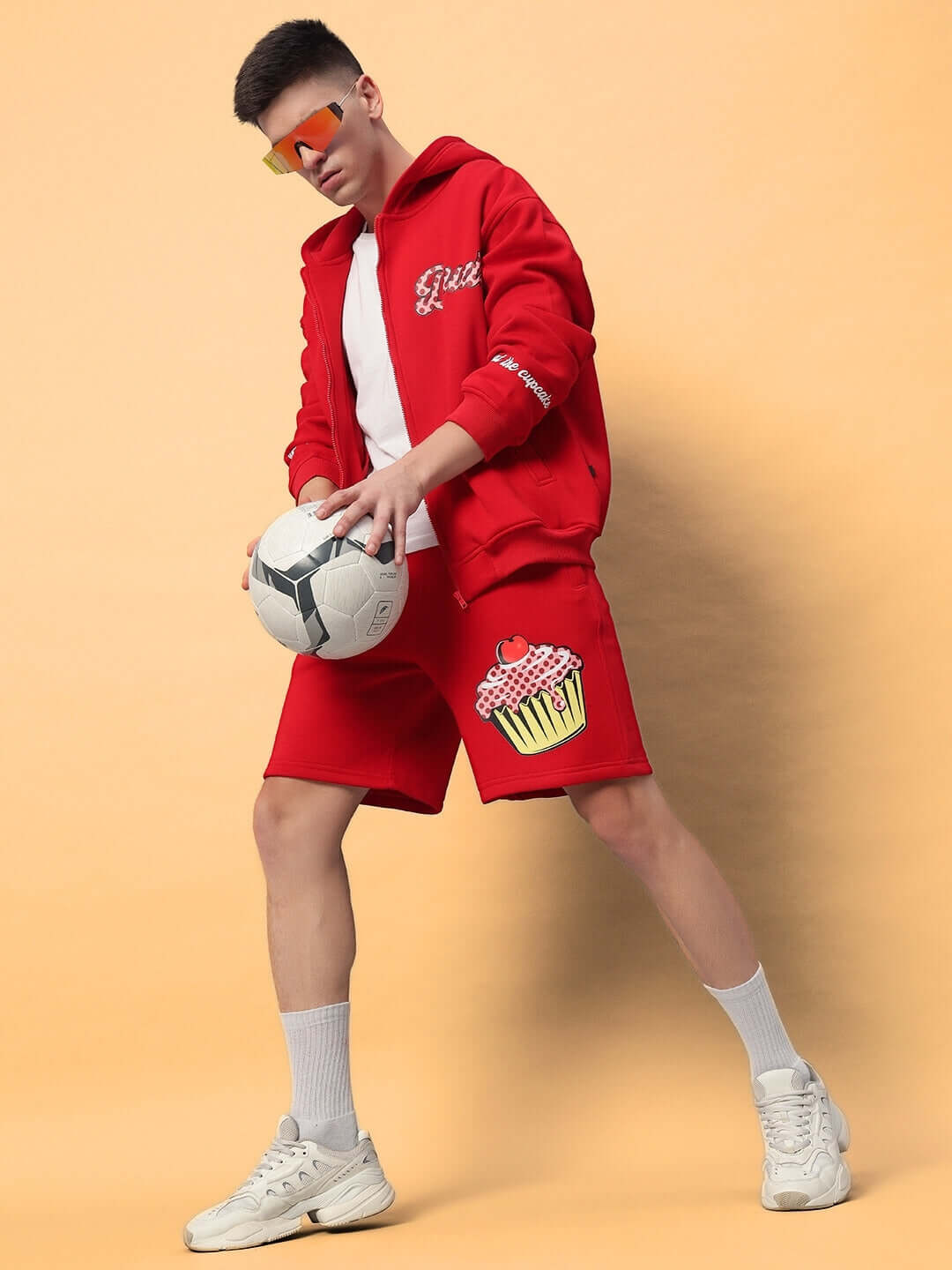 Model wearing the vibrant CUPCAKE COTTON FLEECE HOODIE RED, pairing it with shorts and sneakers, showcasing a bold streetwear style.