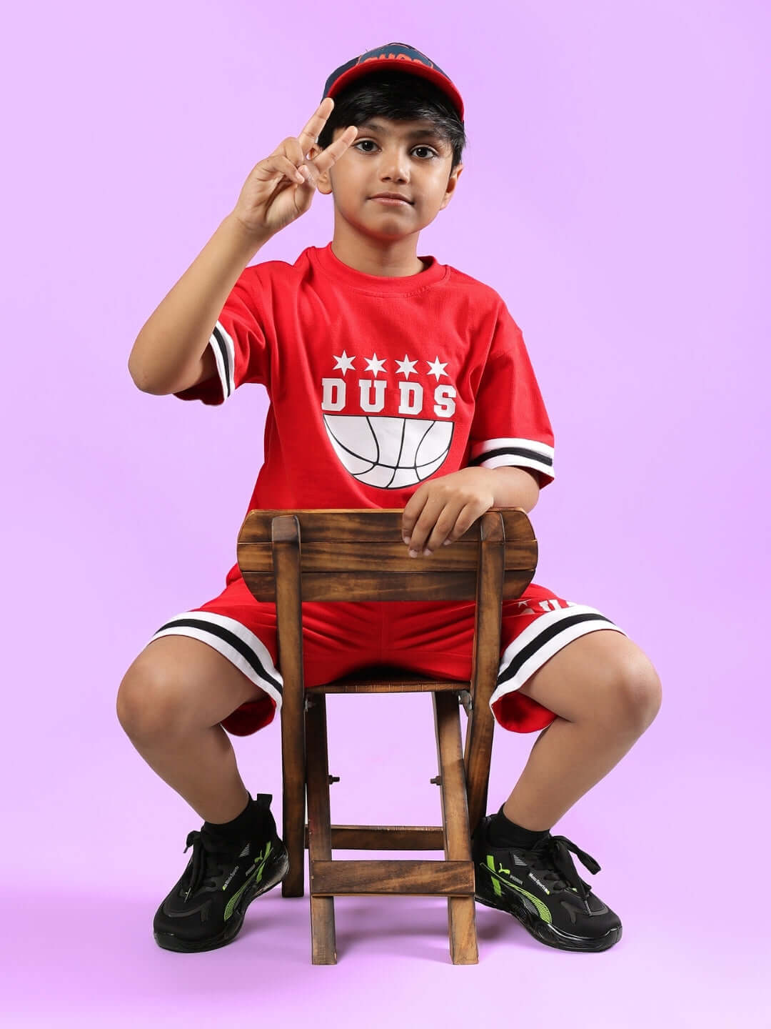 Child in red DIGGIN CO-ORD FOR BOYS & GIRLS set, sitting on a chair, displaying a peace sign. Comfortable DUDS outfit for active kids.