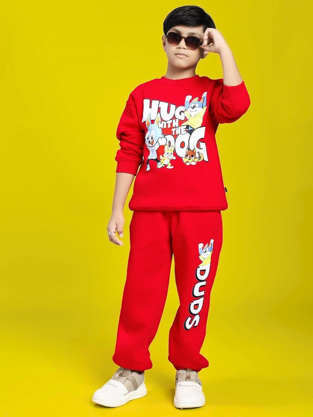 Child wearing HUG WITH THE DOG FLEECE SWEATSHIRT FOR BOYS AND GIRLS RED featuring playful dog print, standing against yellow background.