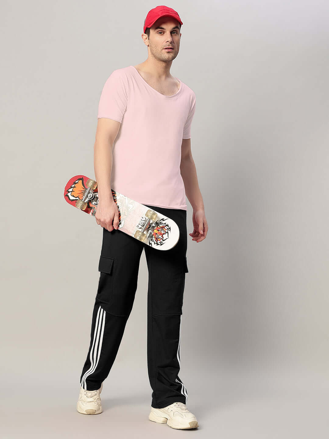 Man in pink t-shirt with skateboard wearing black joggers and red cap.
