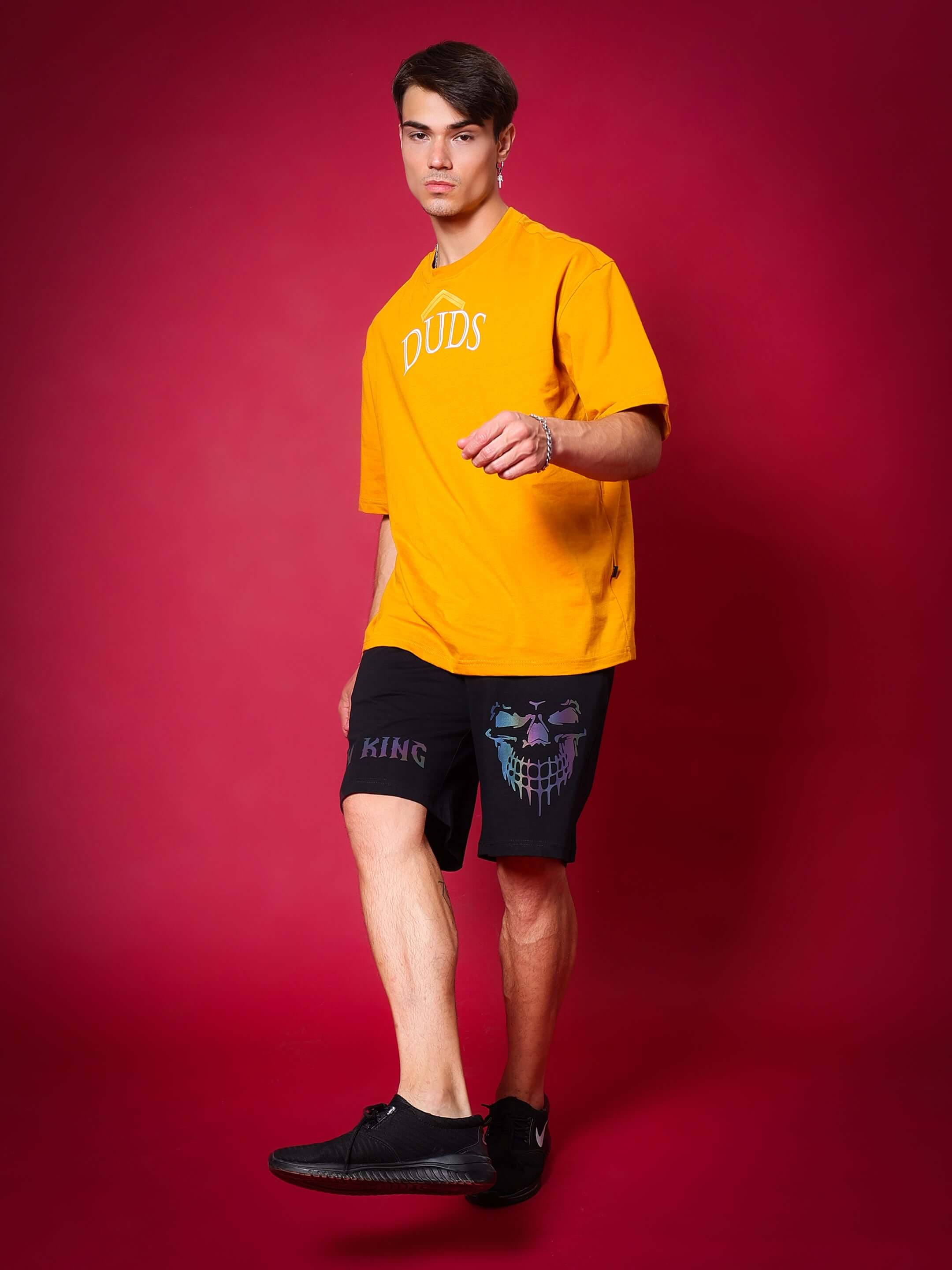 Model wearing Reflector JYM KING Regular Fit Shorts Black with graphic, showcasing stylish activewear on red background.