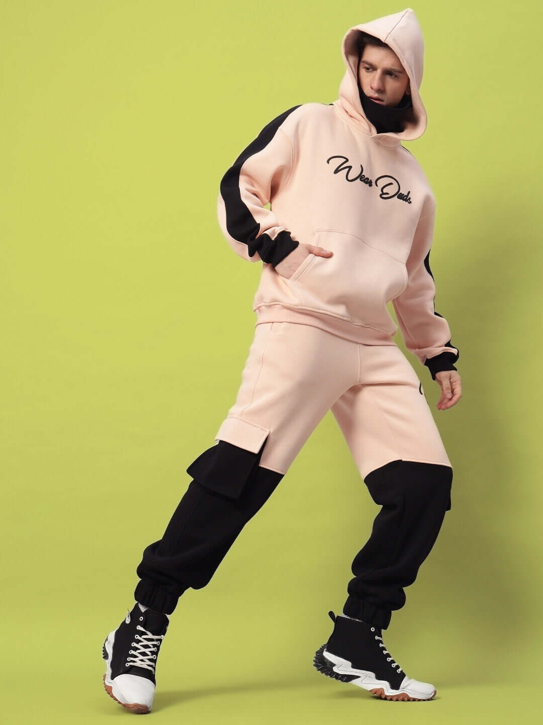 Model wearing REGIMENT FLEECE PANT BEIGE BLACK showcasing contemporary street style with beige base and black accents against green background